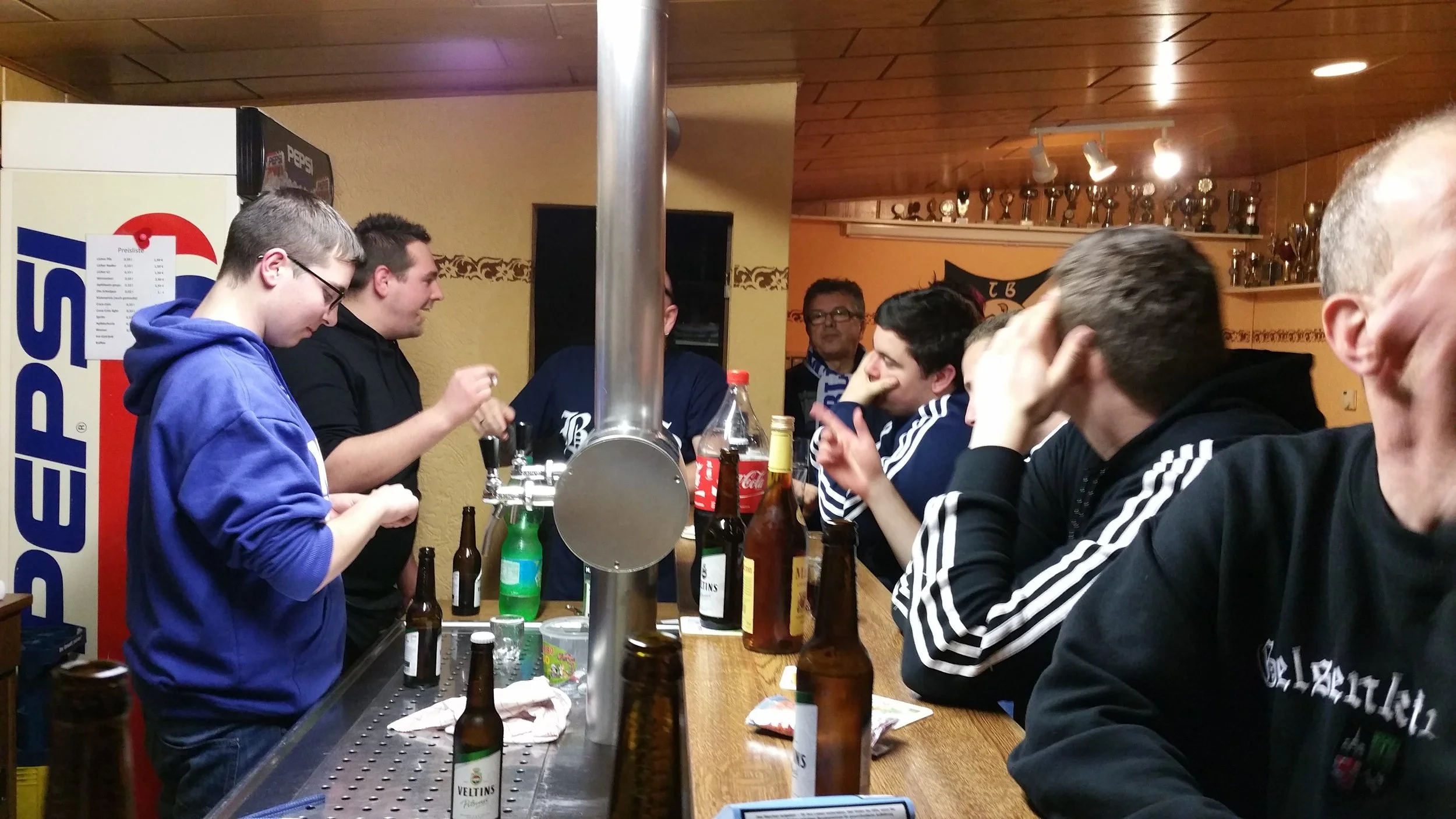 Gruppe junger Männer, die an einer Bar in einem gemütlichen Raum trinken und plaudern, mit mehreren geöffneten Bierflaschen auf dem Tisch.