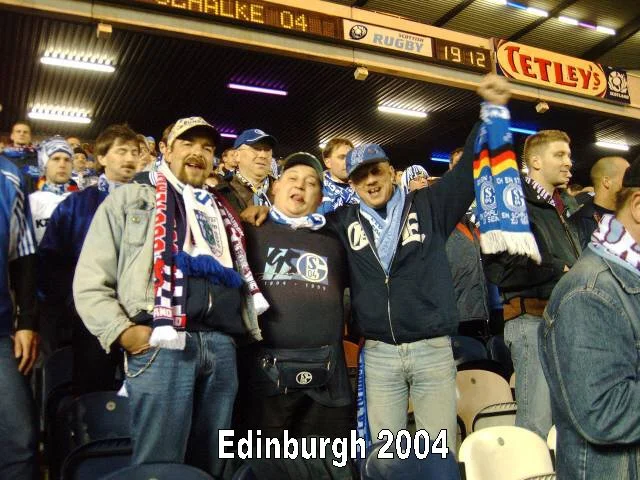 Fußballfans in einem Stadion tragen Schal und Kleidung mit Vereinsfarben, feiern und jubeln bei einem Spiel in Edinburgh 2004.
