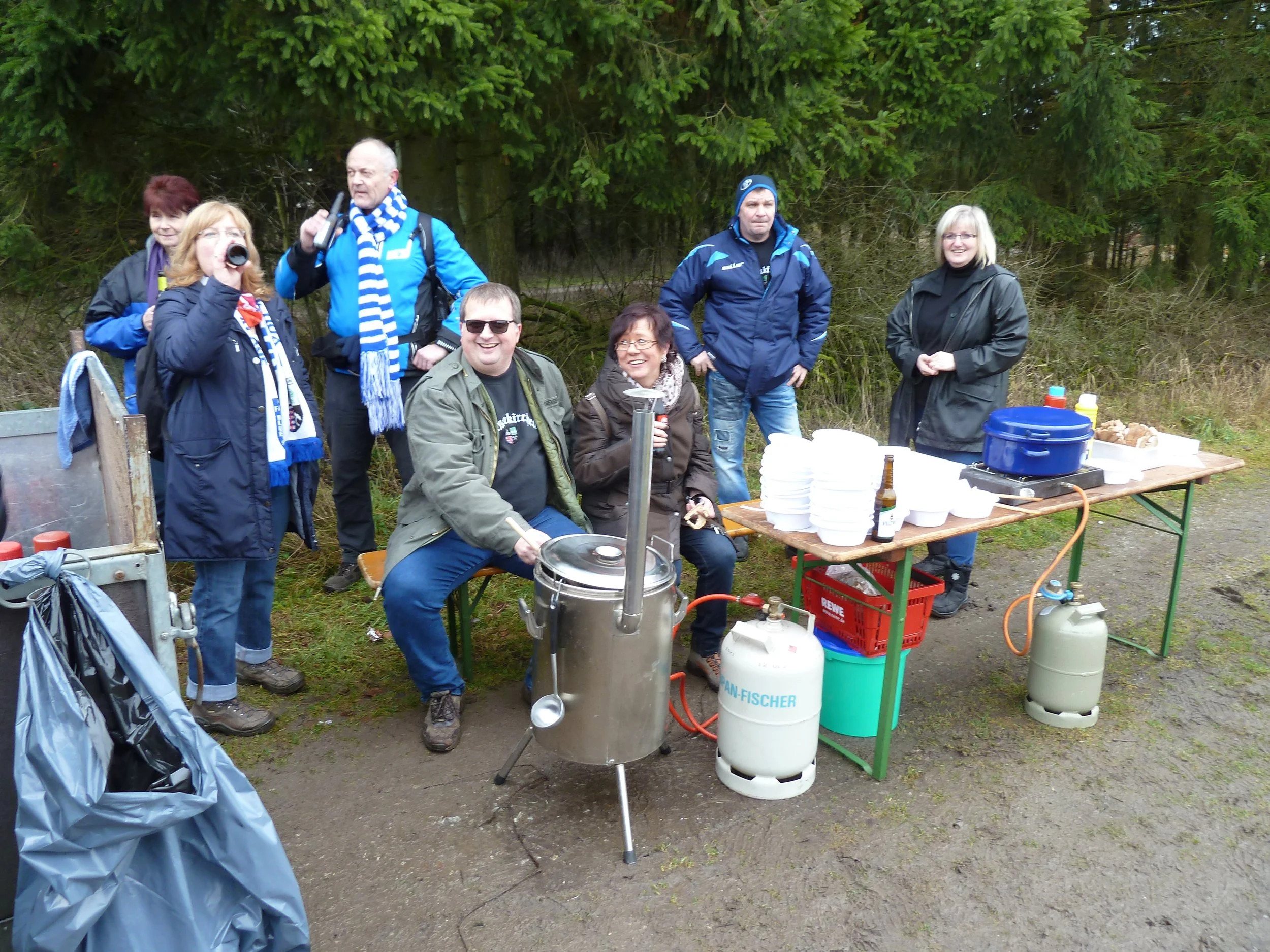 Gruppe von Menschen beim Picknick im Freien, einige lachen, andere schauen interessiert.