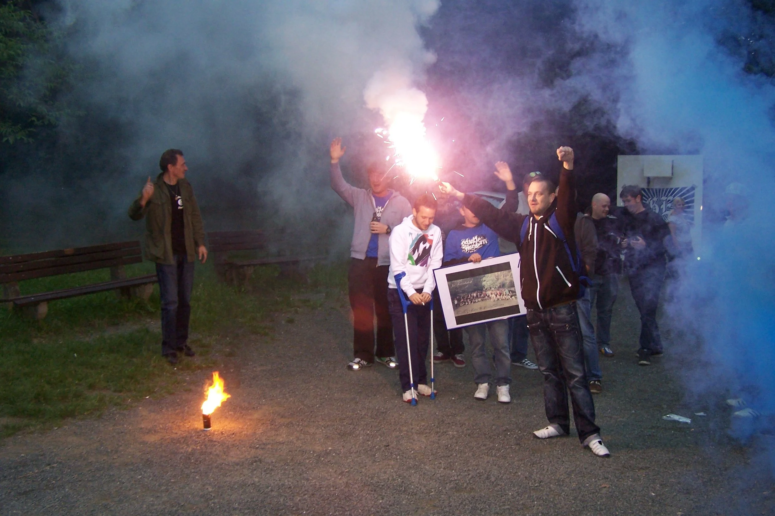 Menschen feiern bei Nacht mit Feuerwerk und Fackeln, Rauch und Feuer sind sichtbar.