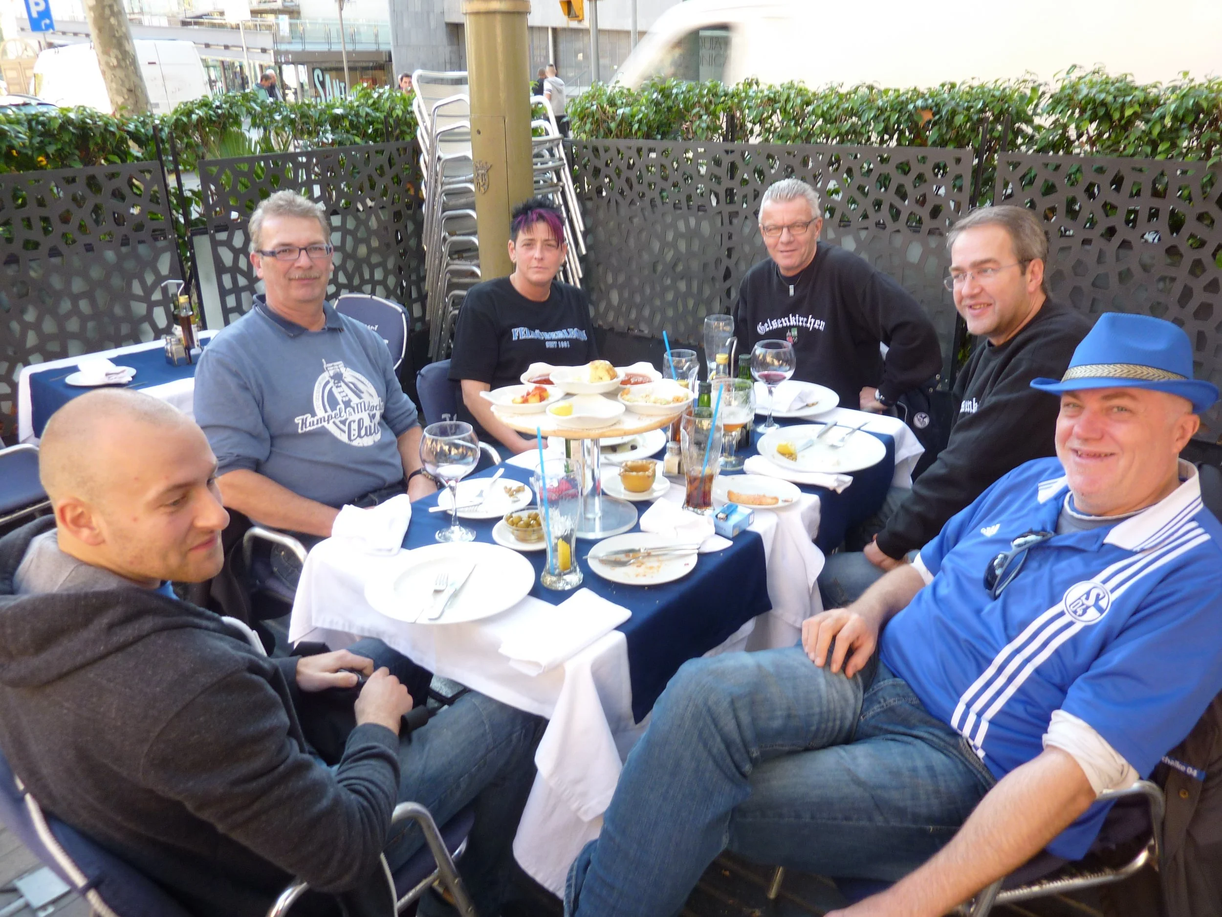 Eine Gruppe von sechs Menschen sitzt bei einem Straßenessen im Freien um einen Tisch.