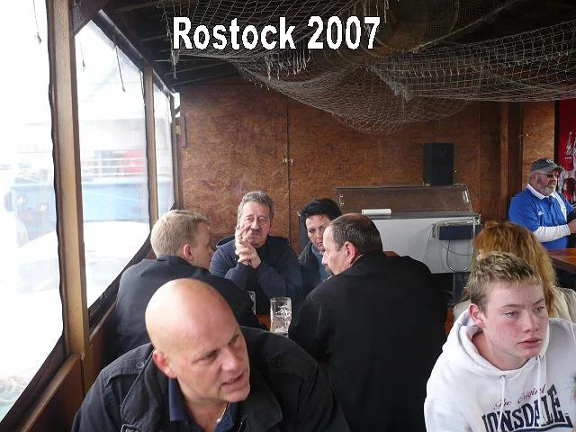 Menschen sitzen in einer Bar oder einem Café in Rostock im Jahr 2007. Sie unterhalten sich, einige trinken. Die Stimmung wirkt entspannt.