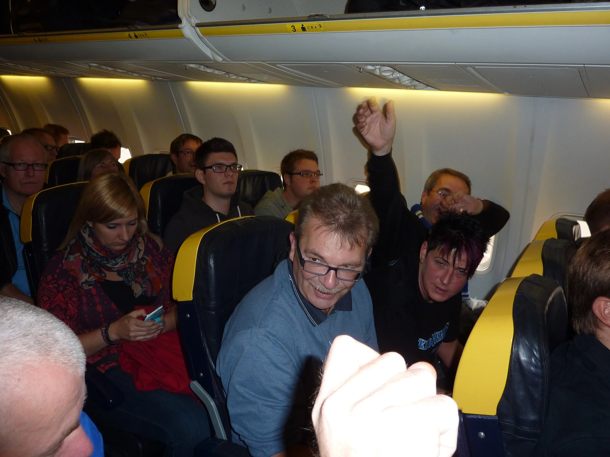 Auf dem Flugzeug sitzen Passagiere, von denen einer die Hand hebt.