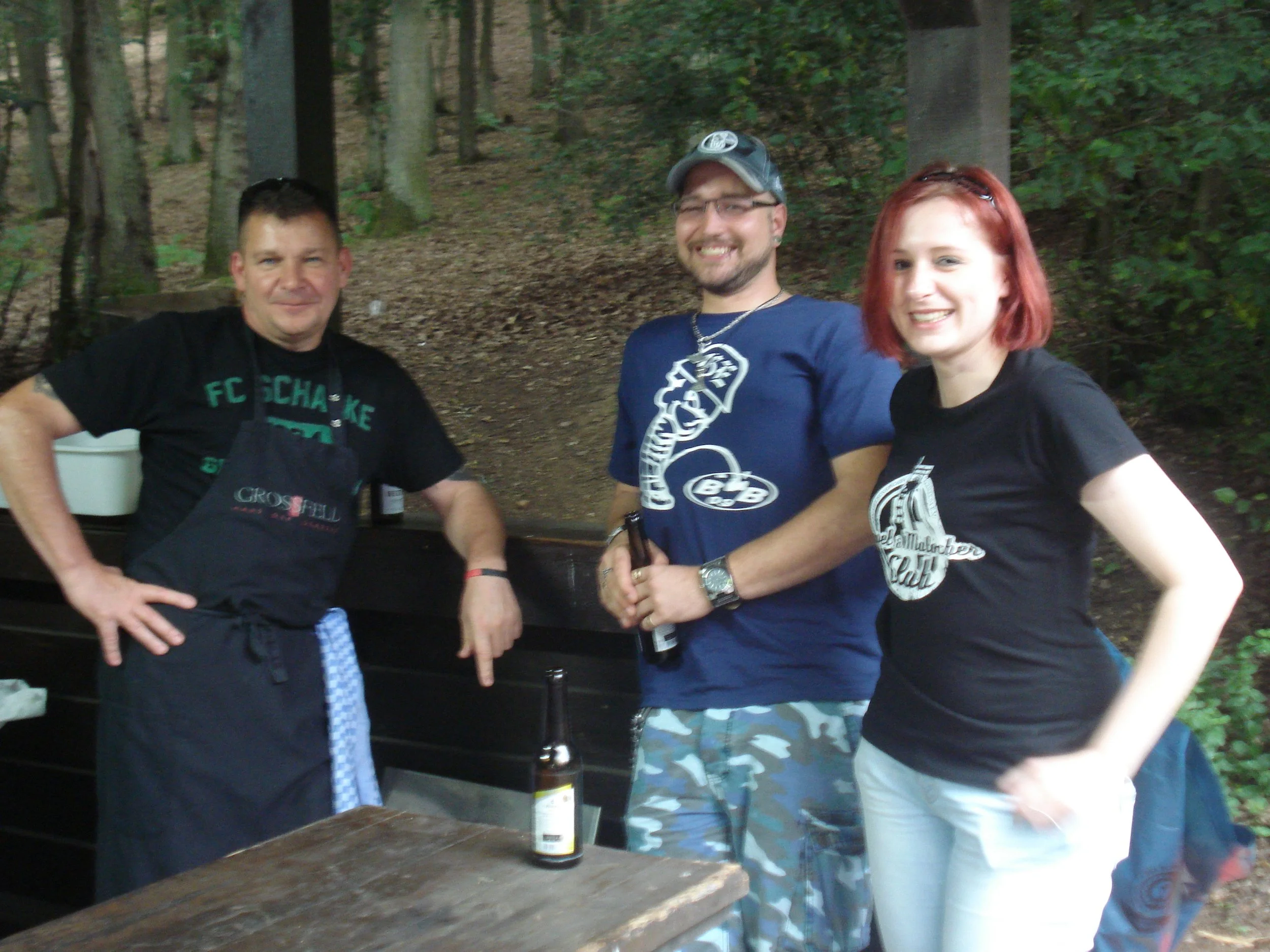 Drei Menschen, die in einem Wald stehen, lachen und posieren für das Foto. Es scheint ein gesellschaftliches Treffen oder ein gemeinsamer Ausflug zu sein.