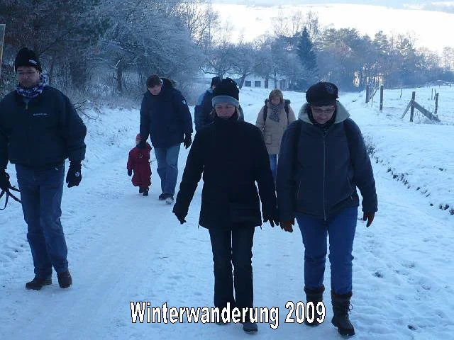 Eine Gruppe von Menschen wandert im Winter auf einem Schneeweg, alle sind warm eingepackt in Jacken und Mützen. Es sind sechs Personen, die offensichtlich bei einer Winterwanderung im Jahr 2009 unterwegs sind.