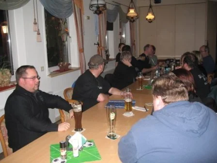 Menschen sitzen an einem langen Tisch in einem Restaurant oder einer Bar, trinken Bier und unterhalten sich.