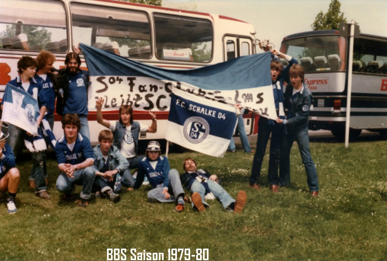 Szene von Fußballfans mit Schals und Fahnen der FC Schalke 04 in einem Park vor Bussen, vermutlich aus der Saison 1979-80.