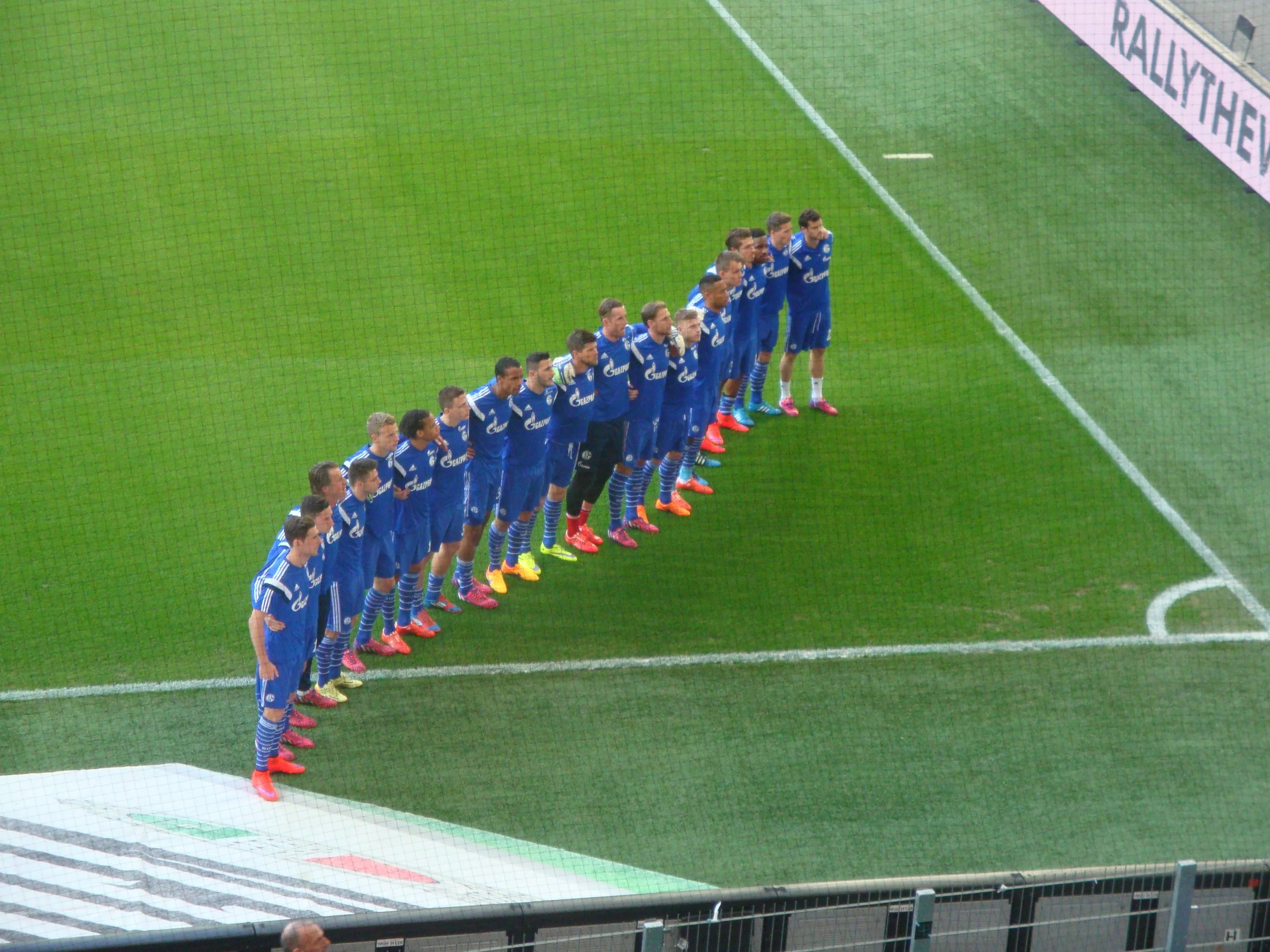 Fußballmannschaft in blauen Trikots steht in einer Reihe vor einem Spielfeld während eines Spiels oder einer Zeremonie.
