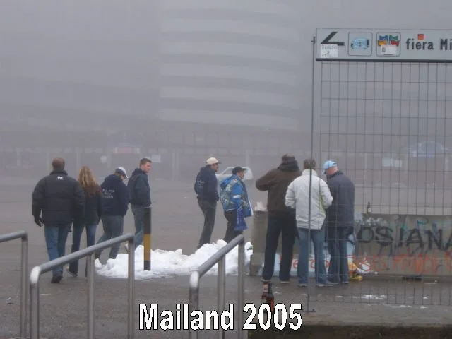 Menschen stehen in einer Gruppe vor einem verschneiten Zaun vor einem modernen Gebäude im Nebel.