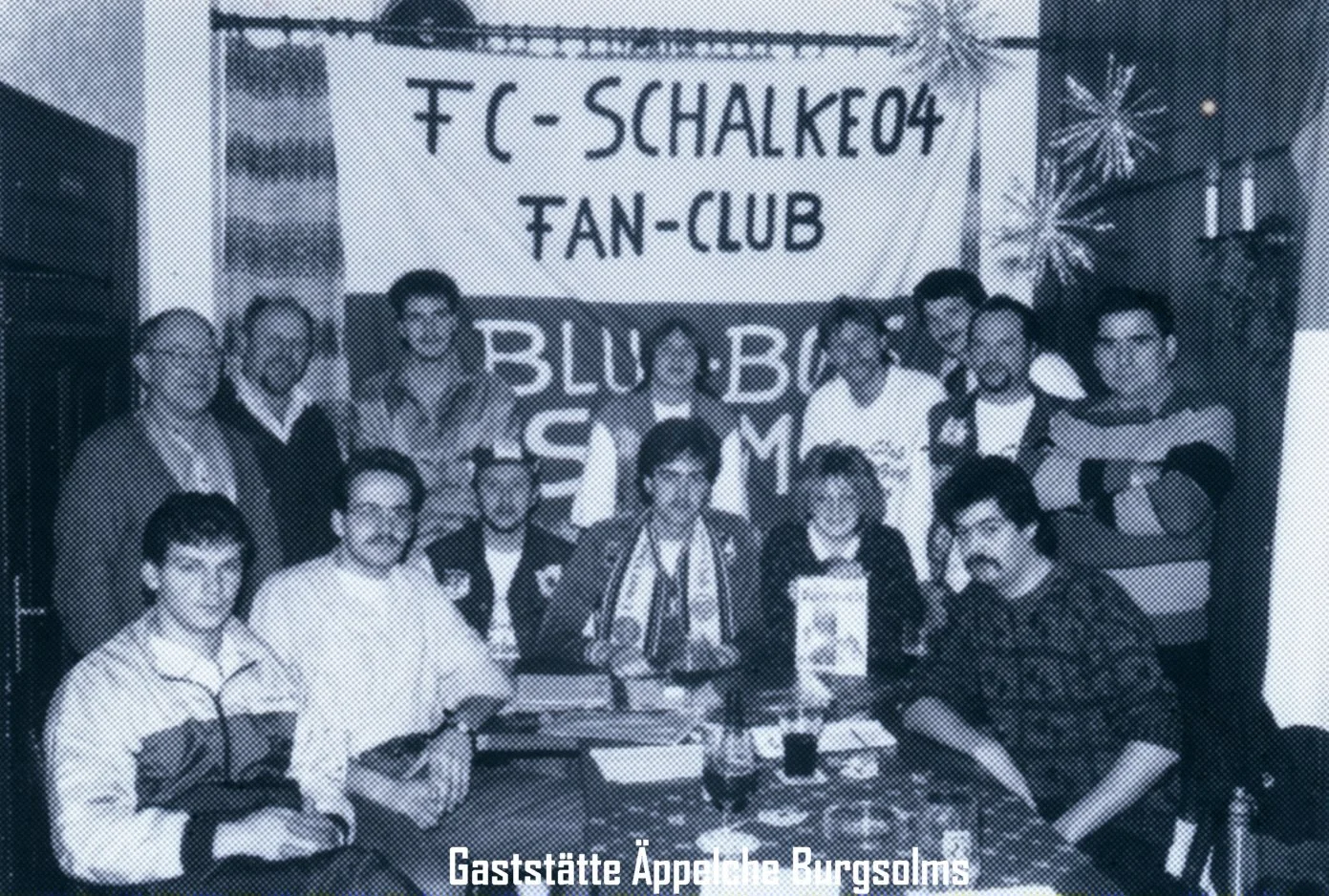 Gruppe von Menschen vor einer Tür mit einem Banner, das den FC Schalke 04 Fan-Club zeigt, im Gasthof Appel in Burgsolms.