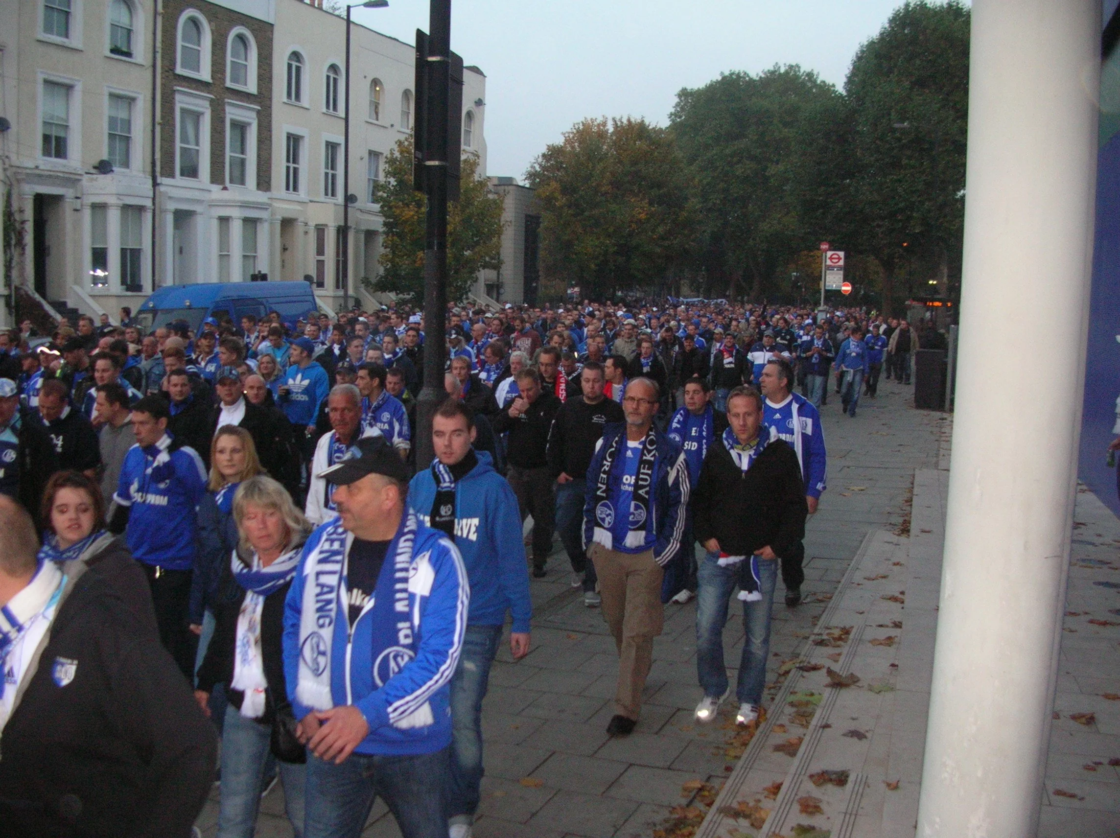 Eine große Gruppe von fußballbegeisterten Menschen trägt blaue Trikots und Schals, wahrscheinlich Fans, die zu einem Spiel oder einer Veranstaltung gehen.