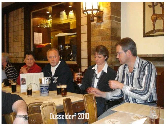 Vier Menschen sitzen an einem Tisch in einem Restaurant in Düsseldorf, 2010, trinken Getränke und sprechen.