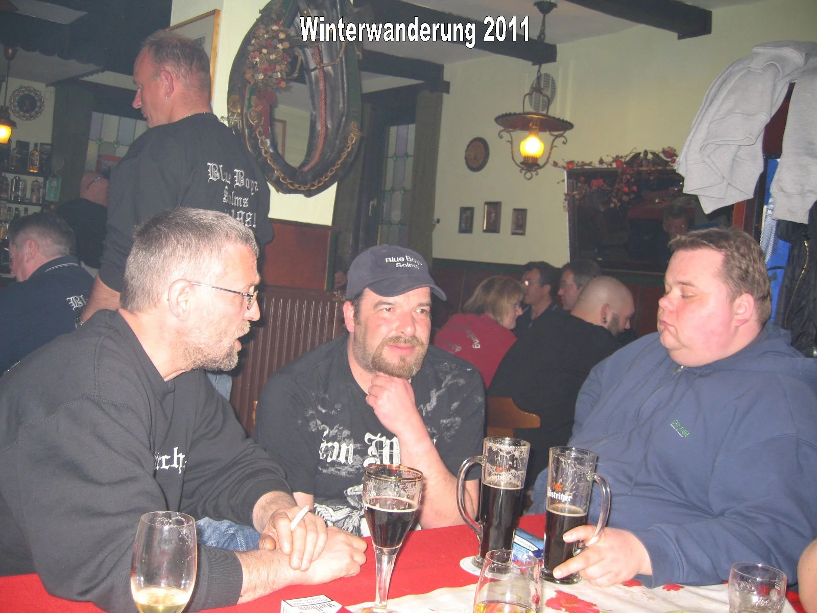 Menschen sitzen in einer Bar, trinken Bier und unterhalten sich. Es ist wahrscheinlich Winter 2011, vermutlich bei einer Winterwanderung, da das Datum im Bild steht.