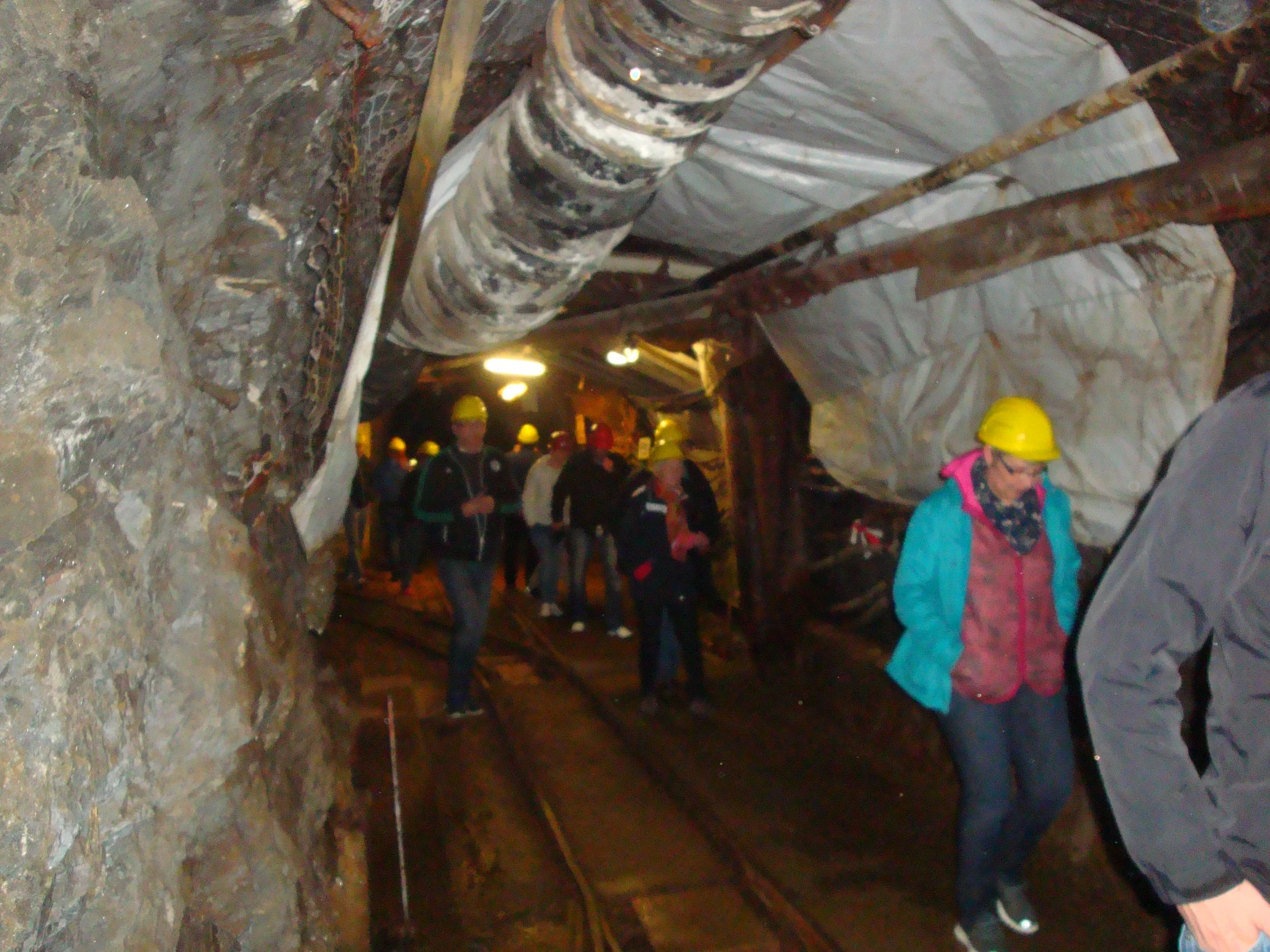 Gruppen von Menschen mit Helmen in einem Bergwerksstollen, Umgebungen aus Felsen und Gestein, Steigbügel und Sicherheitsausrüstung sichtbar.