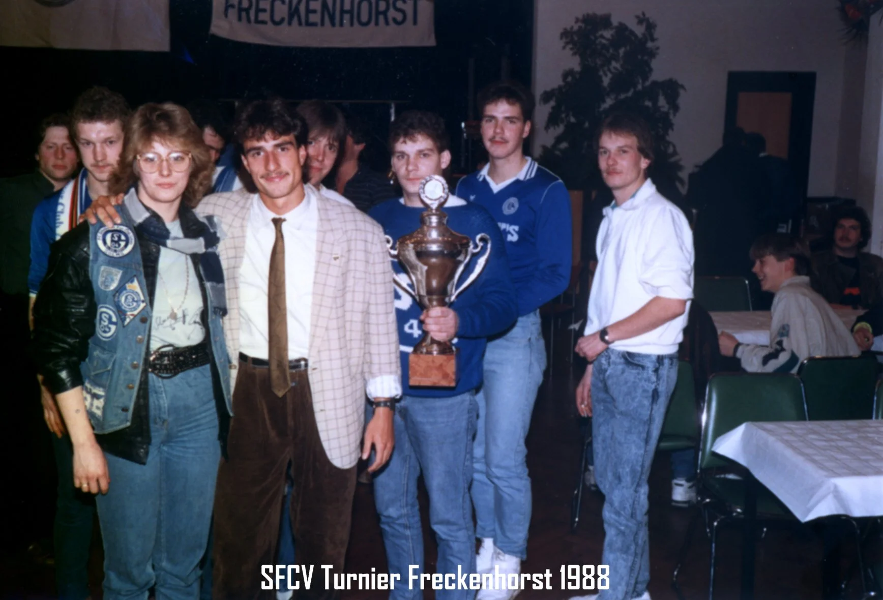Eine Gruppe junger Menschen, die bei einer Siegesfeier eines Turniers im Jahr 1988 in Freckenhorst, vermutlich bei einem Fußballturnier, einen Pokal präsentieren.