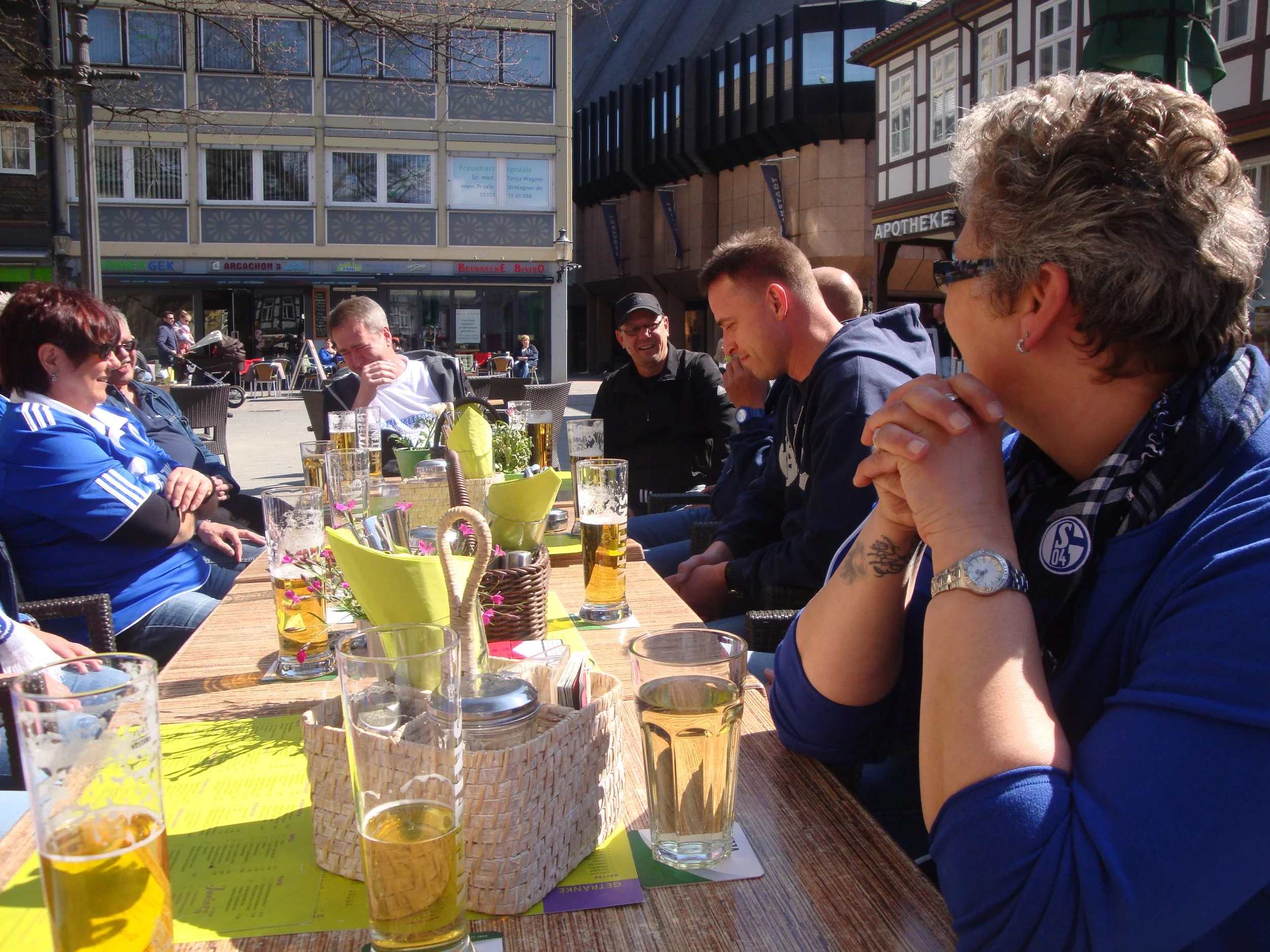 Menschen sitzen an einem Restauranttisch im Freien, während sie Getränke genießen und miteinander sprechen.