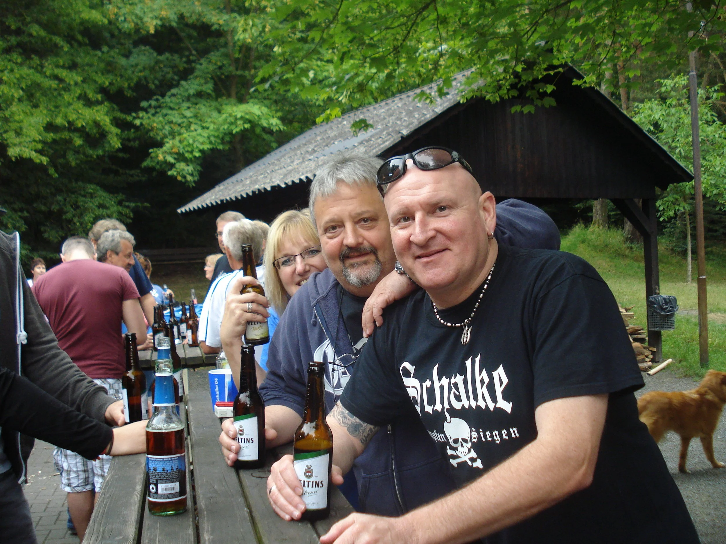 Gruppen von Menschen, die auf einer Outdoor-Party Bier trinken, mit Bäumen im Hintergrund.