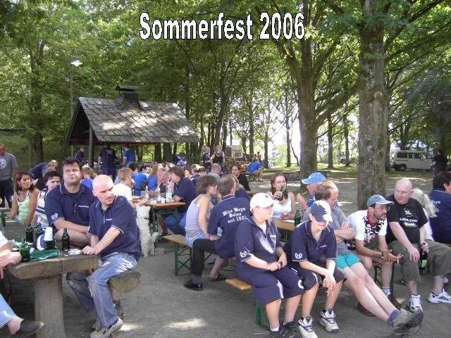 Blick auf eine Gruppe von Menschen, die im Freien bei einem Sommerfest 2006 im Schatten von Bäumen an Tischen sitzen, Getränke trinken und sich unterhalten.