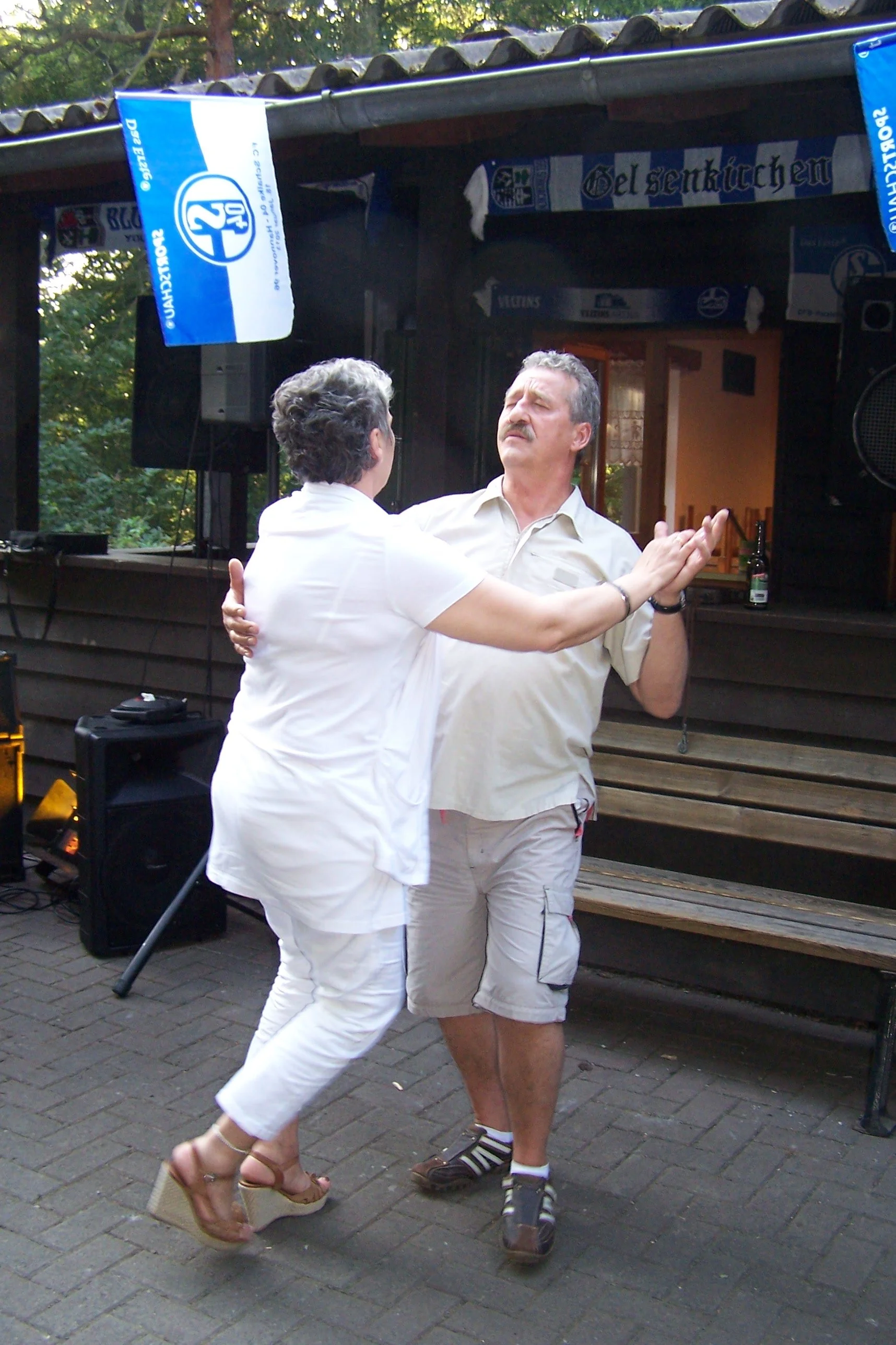 Ein Mann und eine Frau tanzen miteinander im Freien vor einer Bühne, die mit Bierfahnen geschmückt ist.