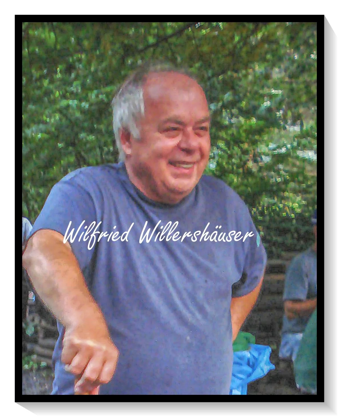 Ein lachender Mann in einem blauen T-Shirt, im Hintergrund Grünflächen und andere Personen, mit dem Text 'Wilfried Willershäuser' auf dem Bild.