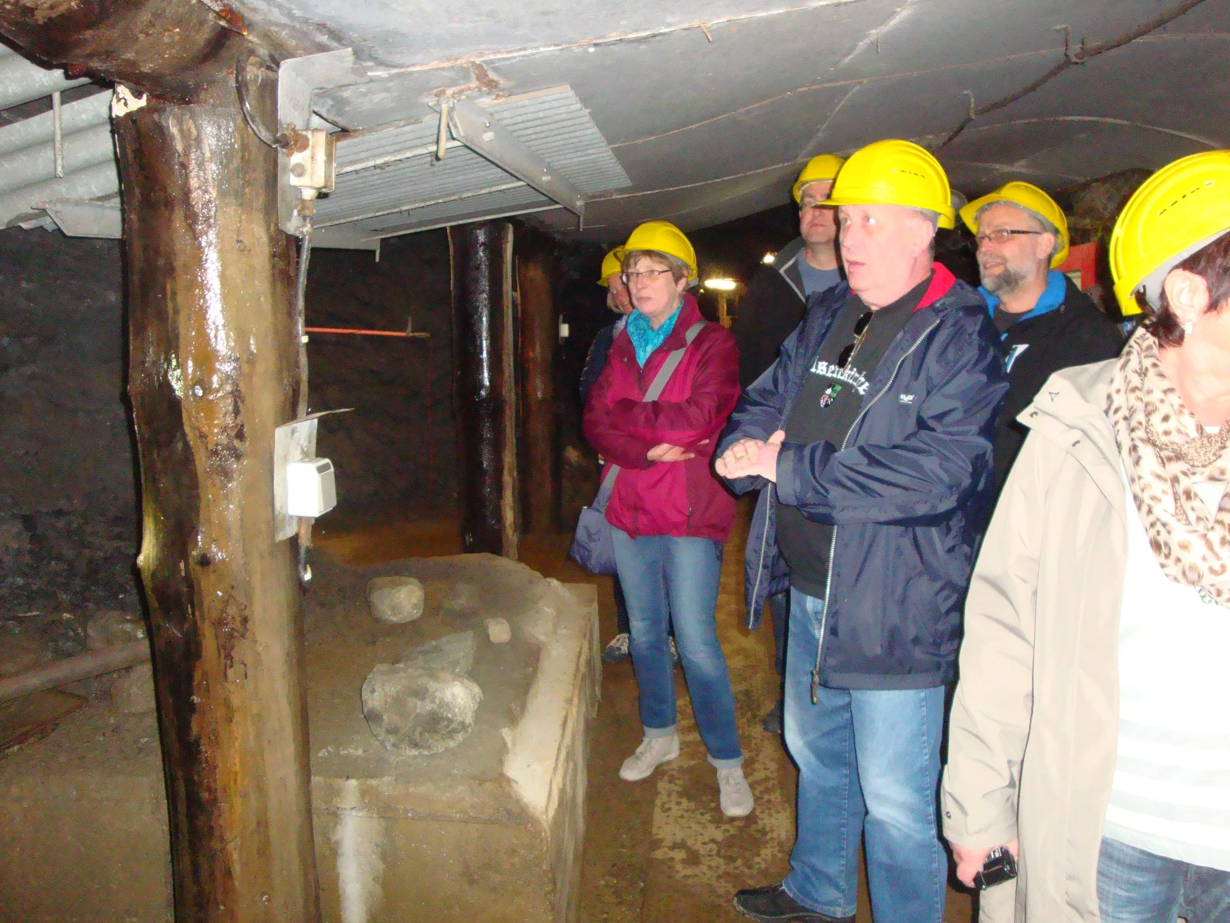 Menschen mit Schutzhelmen besichtigen eine alte Grubenstempel mit Holzstützen in einem Bergwerk.