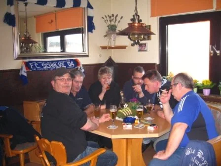 Sechs Menschen sitzen um einen roten Tisch in einem Restaurant, trinken Bier und unterhalten sich.