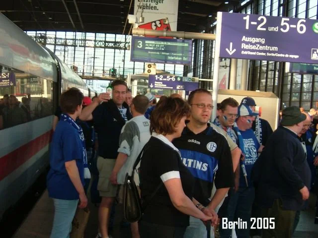 Menschen warten in einem Bahnhof, einige tragen Schal- und Trikots einem Fußballverein in Berlin, 2005.
