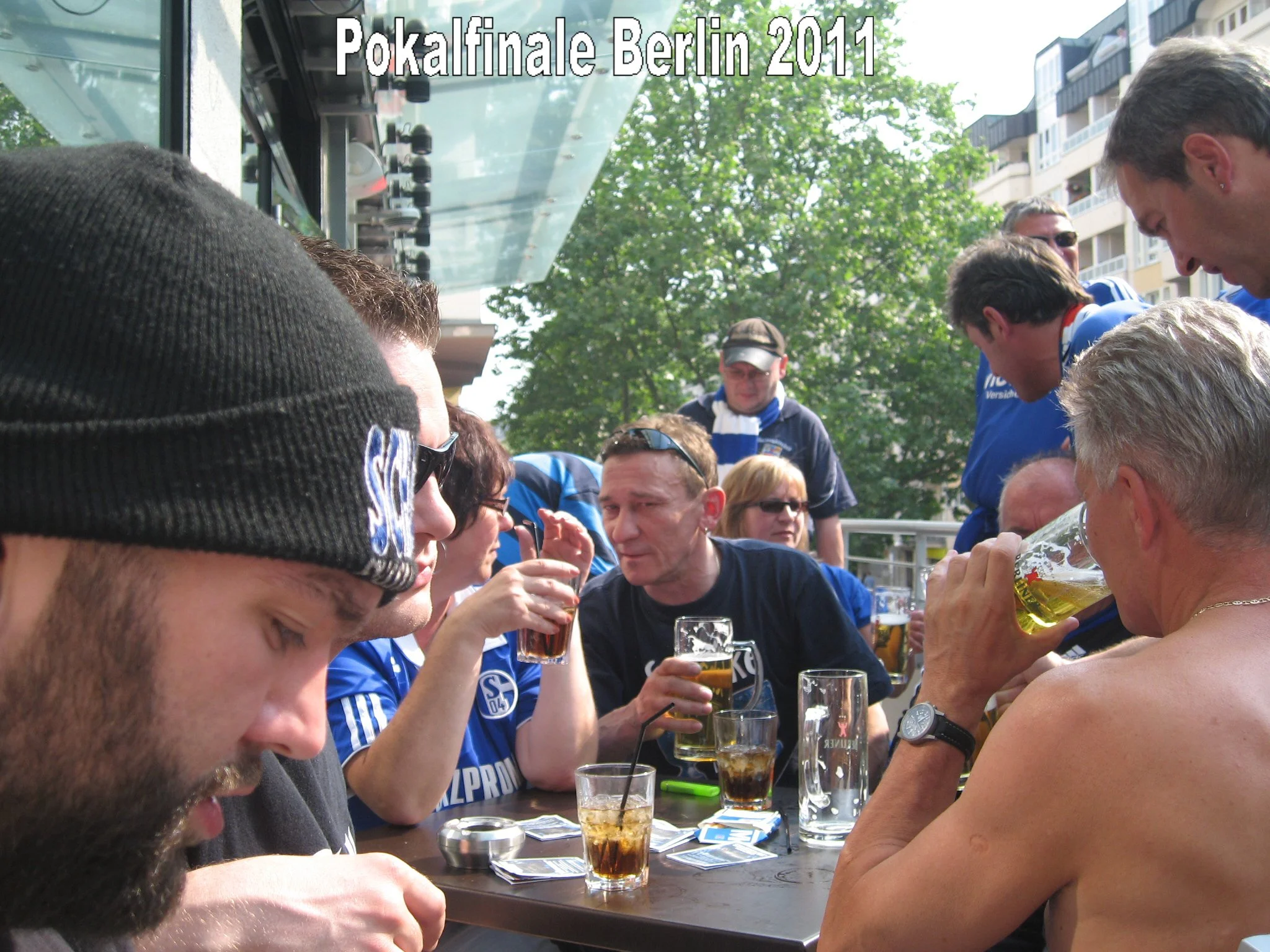 Menschen versammeln sich draußen an einem Tisch, trinken Bier, es ist sonnig und es scheinen Fans eines Fußballteams zu sein, vermutlich während eines Wettkampfs in Berlin 2011.