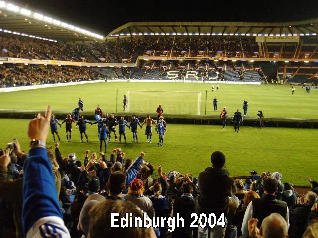 Fußballspiel im Stadion in Edinburgh, 2004, mit Spielern auf dem Feld und Zuschauern im Publikum.
