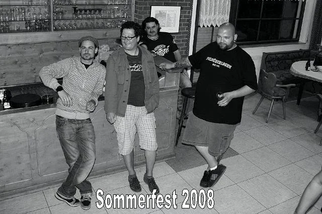 Vier Männer stehen in einer Bar, einige tanzen oder posieren, im Hintergrund ein Tresen mit Gläsern, und es steht der Text 'Sommerfest 2008'.