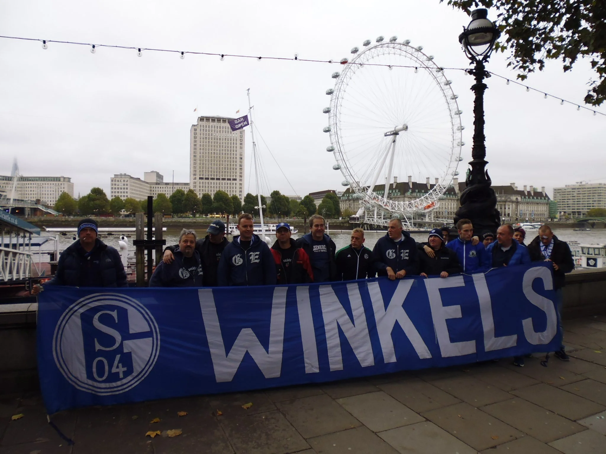 Grupp von Menschen am Fluss in Berlin, im Hintergrund das Riesenrad und Wolkenkratzer.