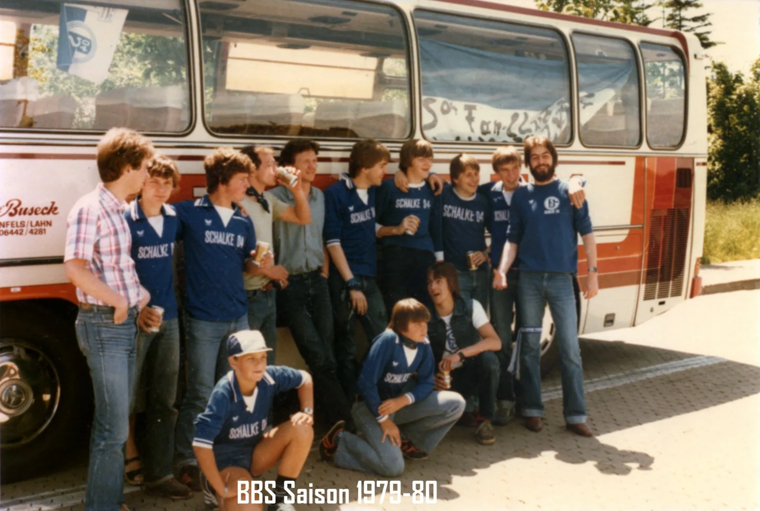 Eine Gruppe junger Männer und Jungen steht vor einem roten Bus, einige tragen blaue Trikots mit der Aufschrift 'Schalke 04'. Es ist eine Fotoszene aus der Saison 1979-80.