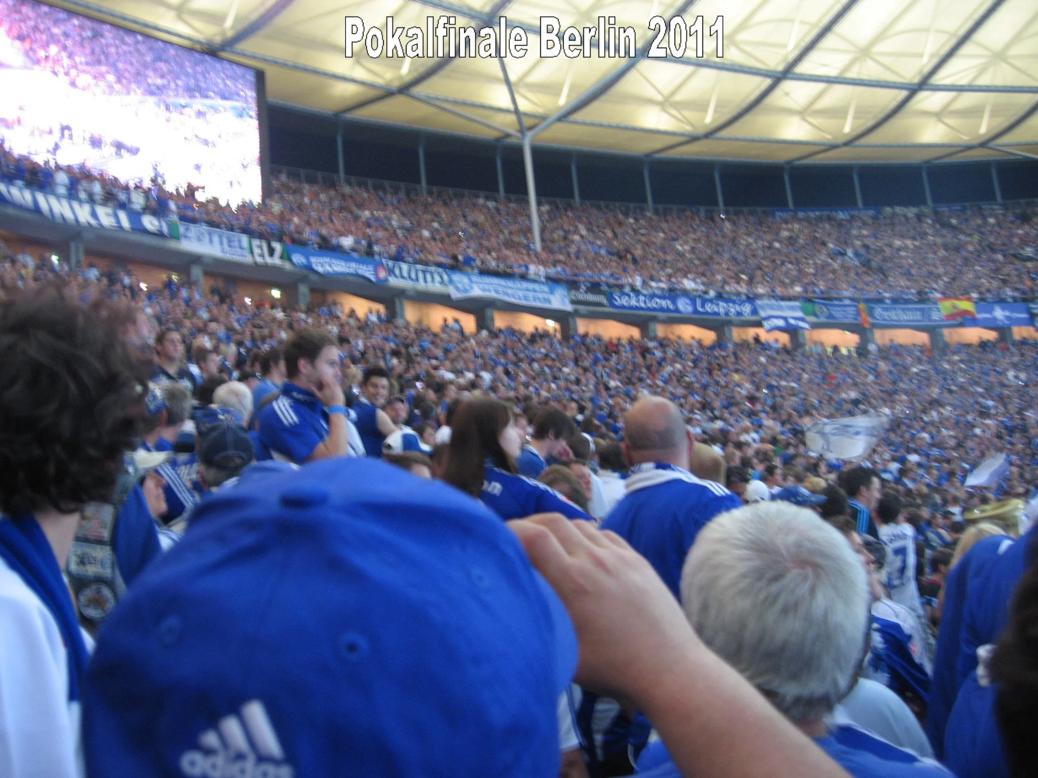 Blick in ein überfülltes Fußballstadion während der Pokalfinalen in Berlin 2011, voller Fans in blauen Trikots, mit einer großen Video-Übertragung im Hintergrund.