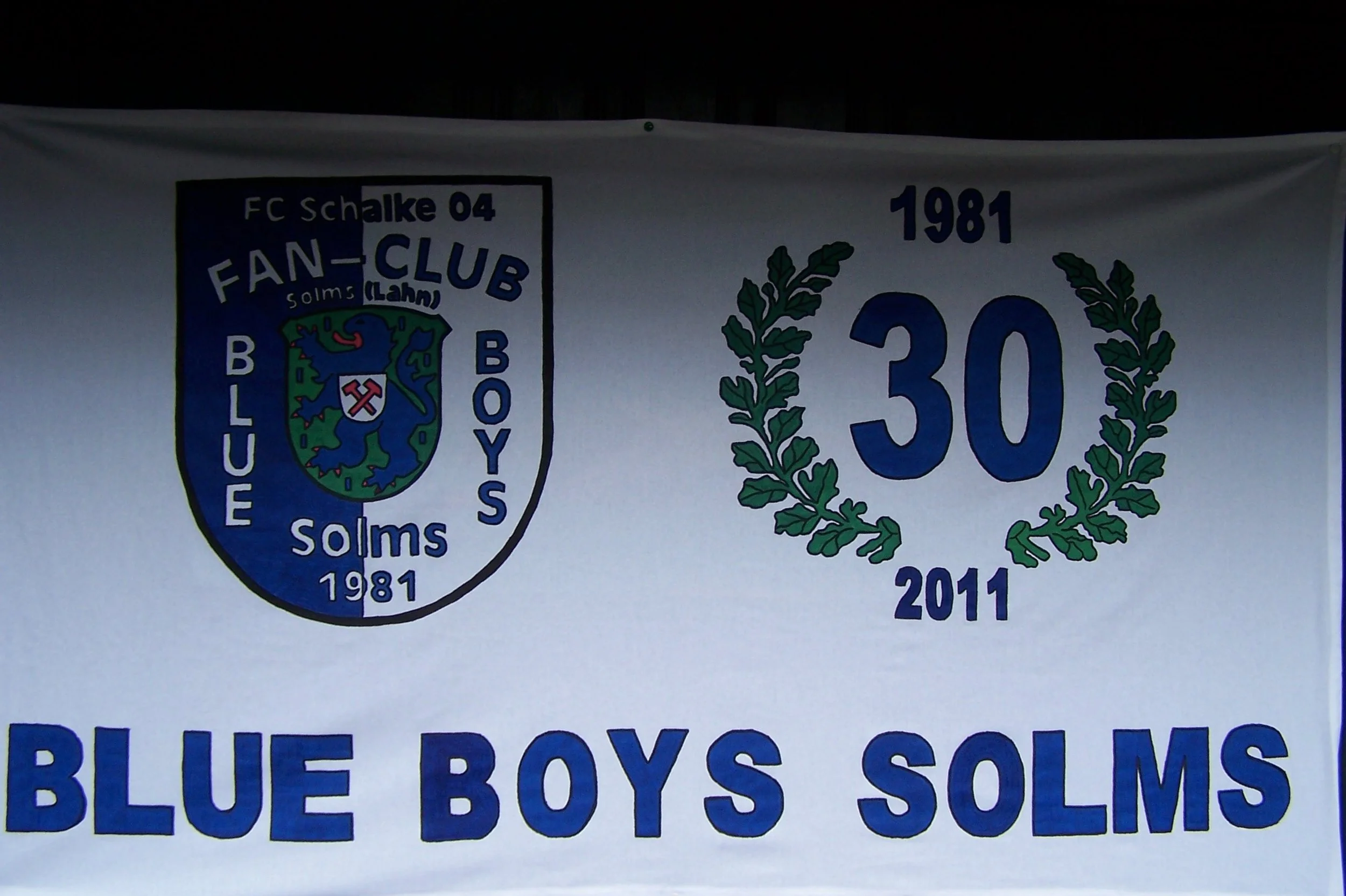 Wappen und Text auf einer weißen Fahne, die den FC Schalke 04 Fan-Club Solms e.V. zeigt, mit den Jahren 1981 und 2011 und der Aufschrift »Blue Boys Solms«.