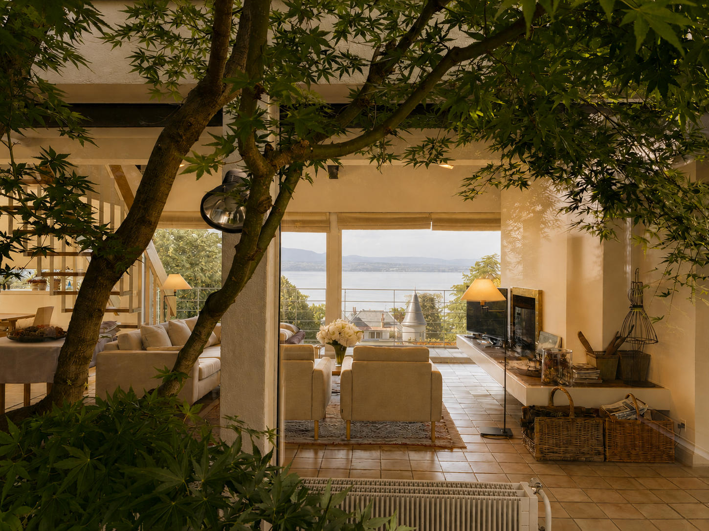 Salon intérieur avec un arbre et vue sur un lac depuis la fenêtre.