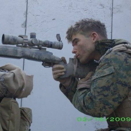 Thomas Thatcher, the owner of Say Less Fight Club, sitting behind a scoped rifle as a Marine Corps Scout Sniper while serving in Kaneohe Bay, Hawaii.