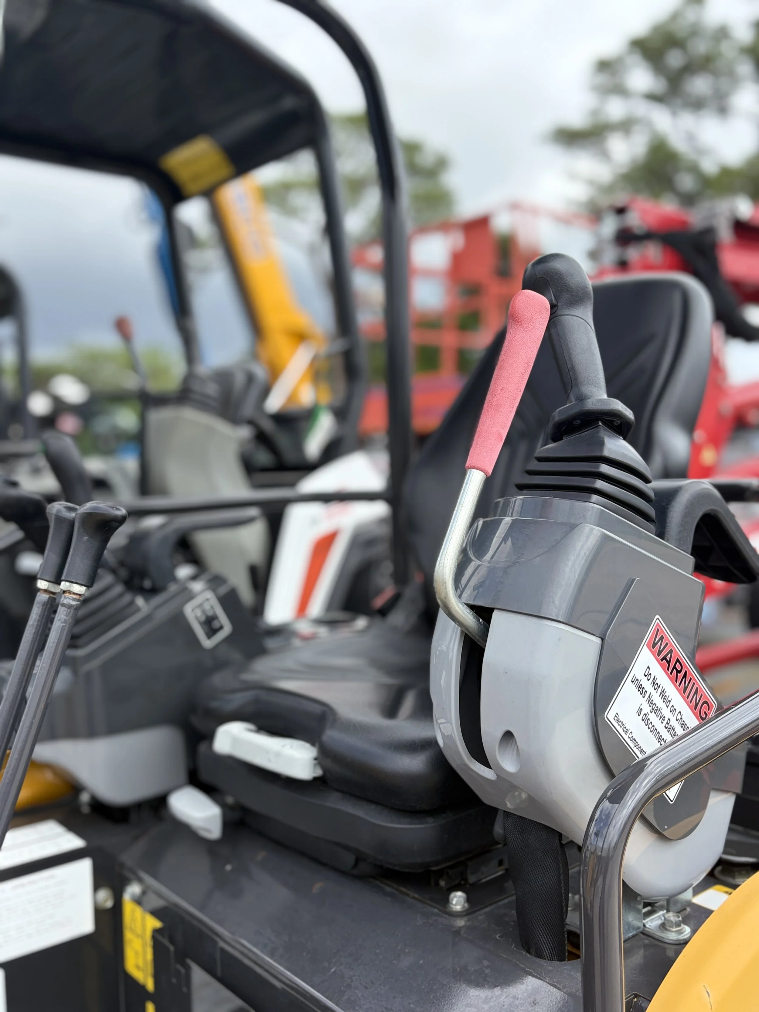 Close-up of electric golf cart motor and battery compartment, with warning label and electrical components, outdoors with trees and other golf carts in the background