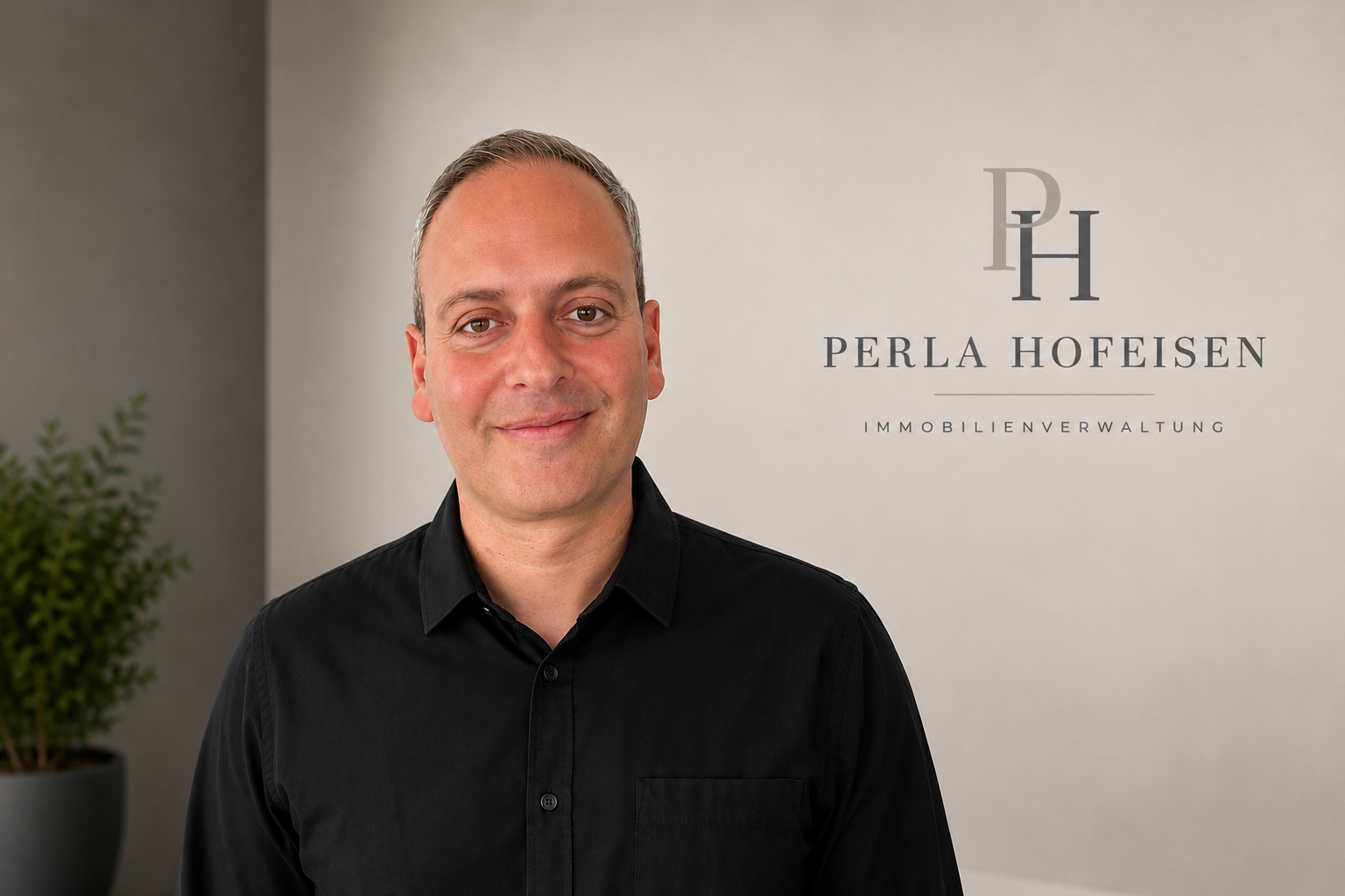 Ein Mann in schwarzem Hemd steht vor einer Wand mit dem Logo und dem Namen 'Perla Hofeisen Immobilienverwaltung' in Photoshop-Design.