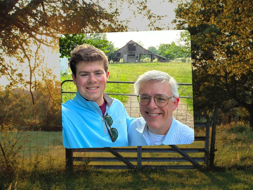 A billboard located outdoors on a rural farm, displaying a photo of two smiling men in front of a green pasture and barn.