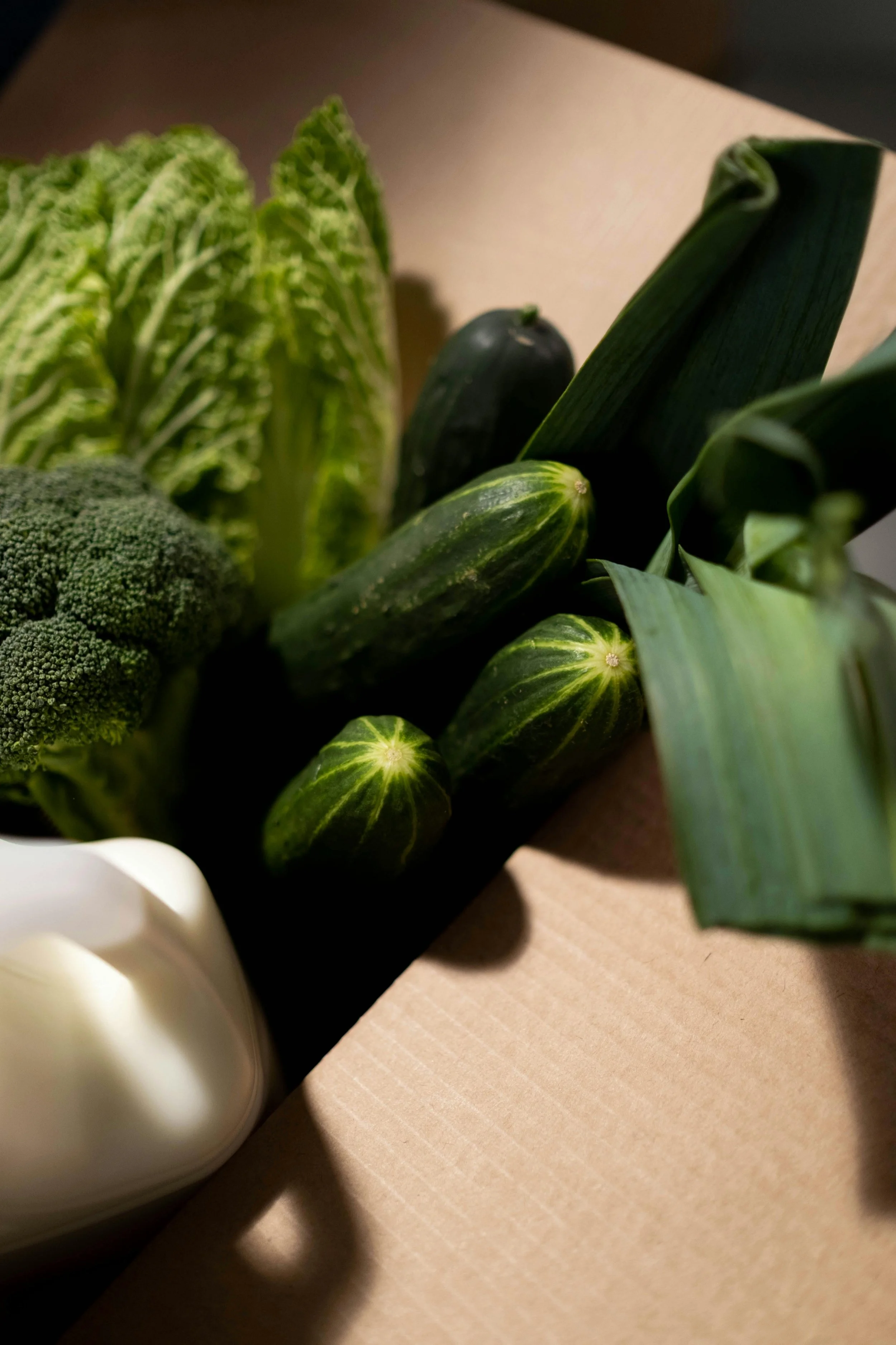 Close-up of fresh green vegetables, including zucchini, lettuce, and possibly broccoli, on a light-colored surface.