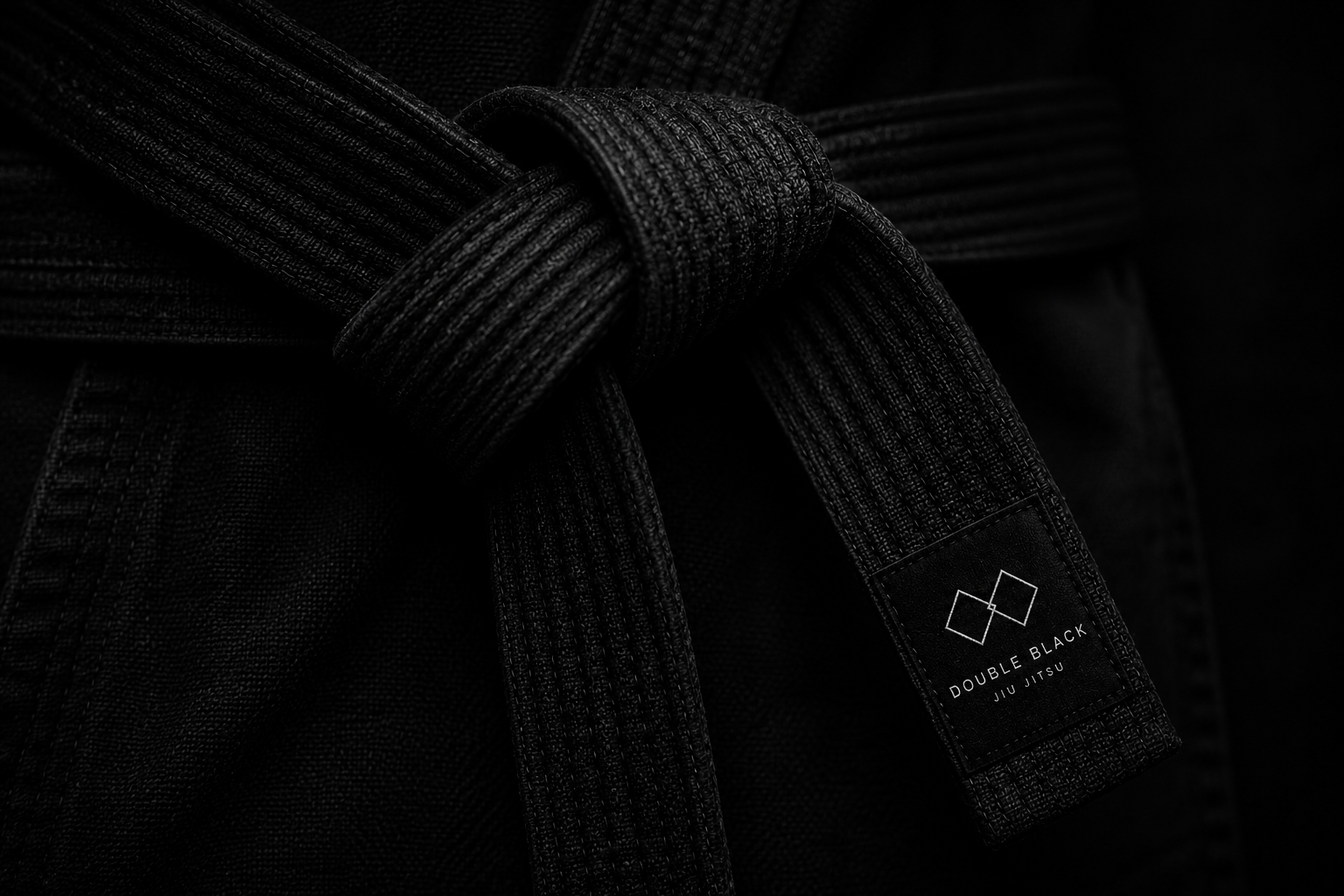 Close-up of a black Brazilian Jiu Jitsu gi with a black belt tied in a knot. The belt has a label that reads 'Double Black Jiu Jitsu' with two overlapping squares logo.
