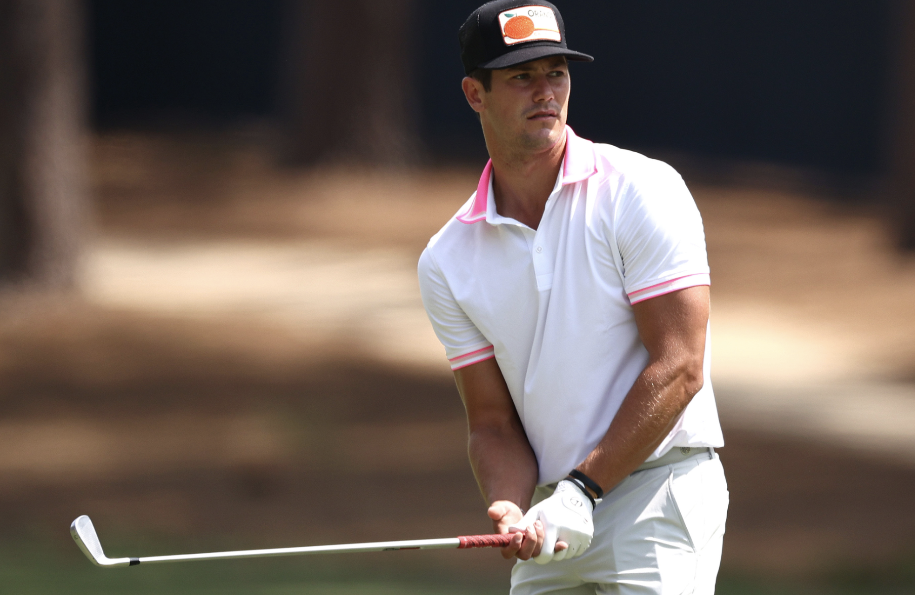 A man dressed in a white golf outfit holding a golf club on a golf course, with a focused expression.