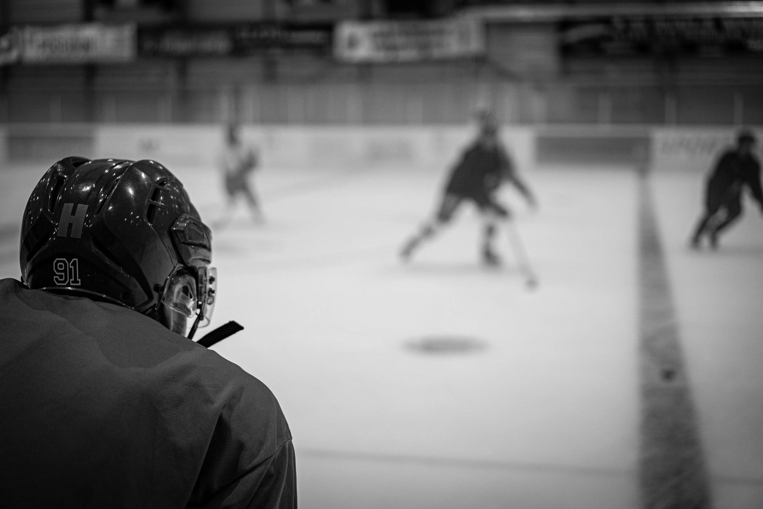 A hockey player in a helmet is watching a game on the ice rink, where several players are skating and playing.
