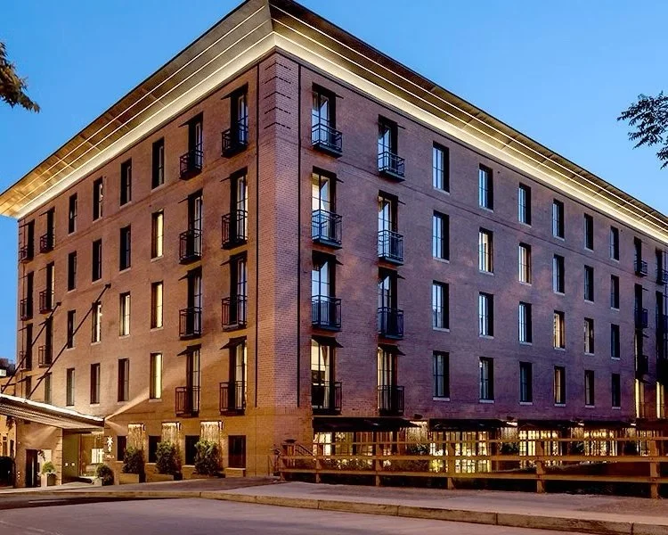 Exterior view of a multi-story brick building with multiple windows and small balconies, illuminated at dusk.