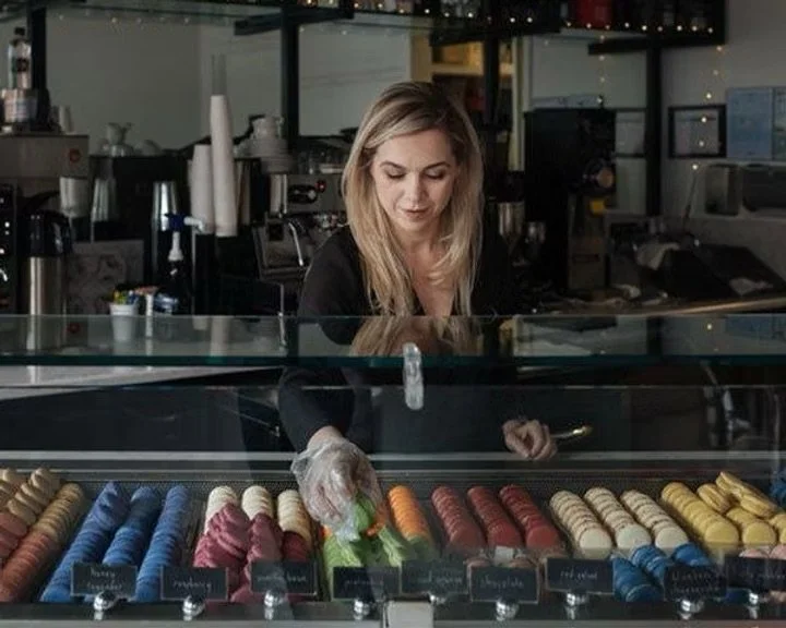 Female business owner grabbing macarons from a glass display.