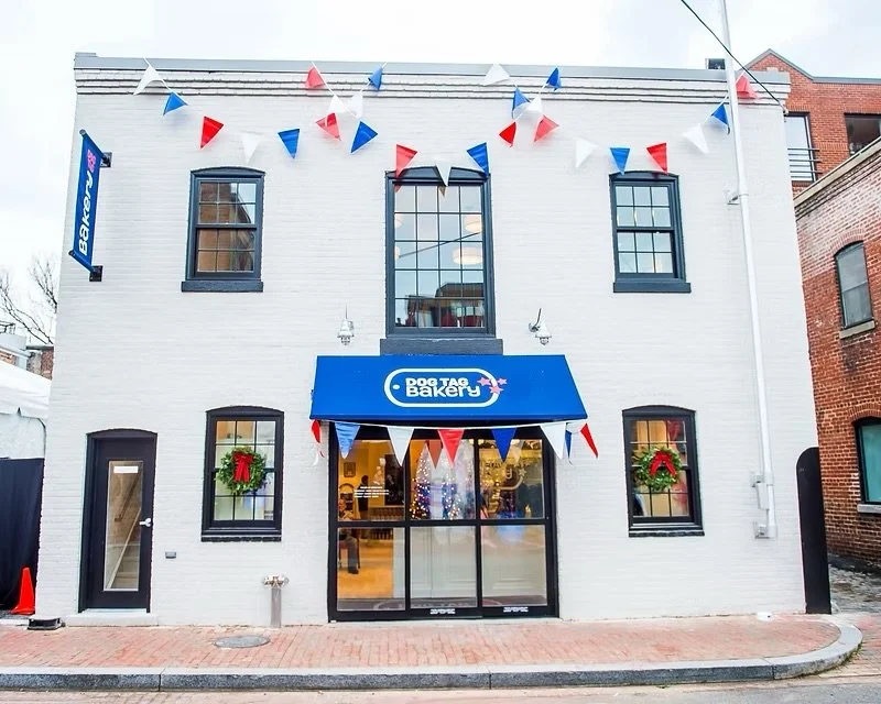Front view of a bakery called 'Dog Tag Bakery' with festive decorations, including wreaths and red, white, and blue pennant banners.
