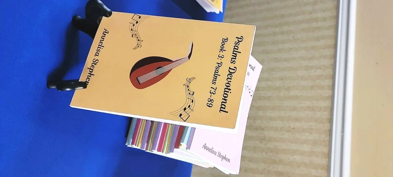 A stack of books on a blue table, with the top book titled 'Psalms Devotional Book 3: Psalms 73-89' by Antleisa Stephen, featuring a guitar illustration on the cover.