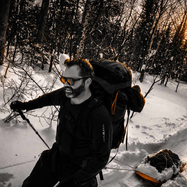 a man backpacking through the snow carrying a sled behind him