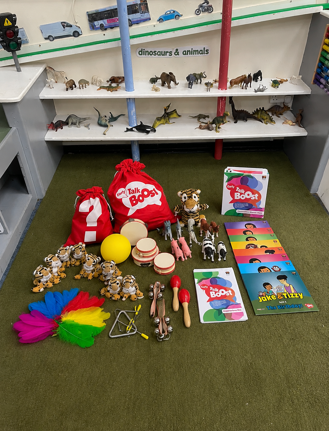 Kids' toys and party supplies for a birthday celebration, featuring toy animals, feather fans, musical instruments, and party books, with a display of toy animal figurines on shelves behind them.