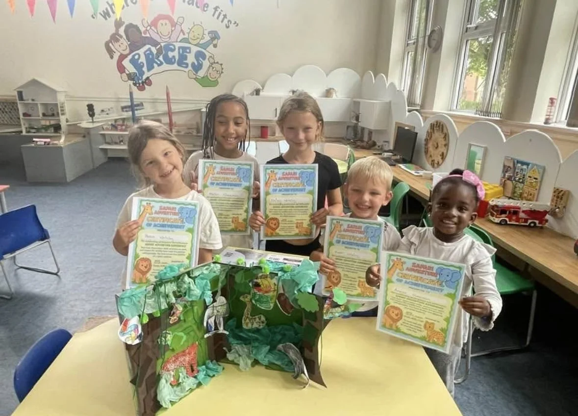Five children holding certificates in after school club  with jungle animal decorations and a jungle-themed diorama on the table.